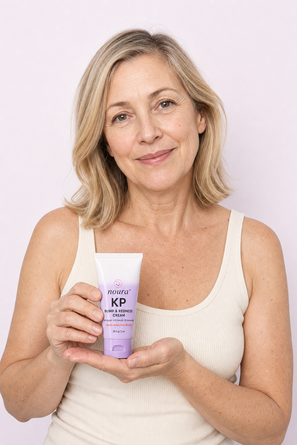 Smiling woman in a white tank top holding a tube of Noura KP Bump & Redness Cream