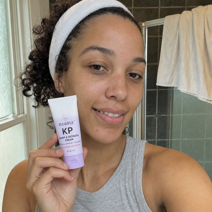 Woman with curly hair and a white headband holding a tube of Noura KP cream in her bathroom