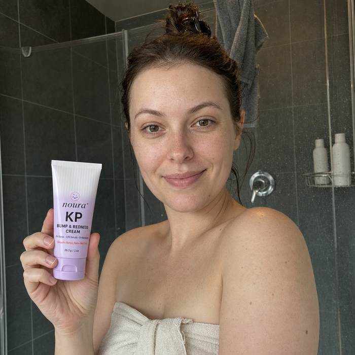 Woman wrapped in a towel holding a tube of Noura KP cream in the bathroom