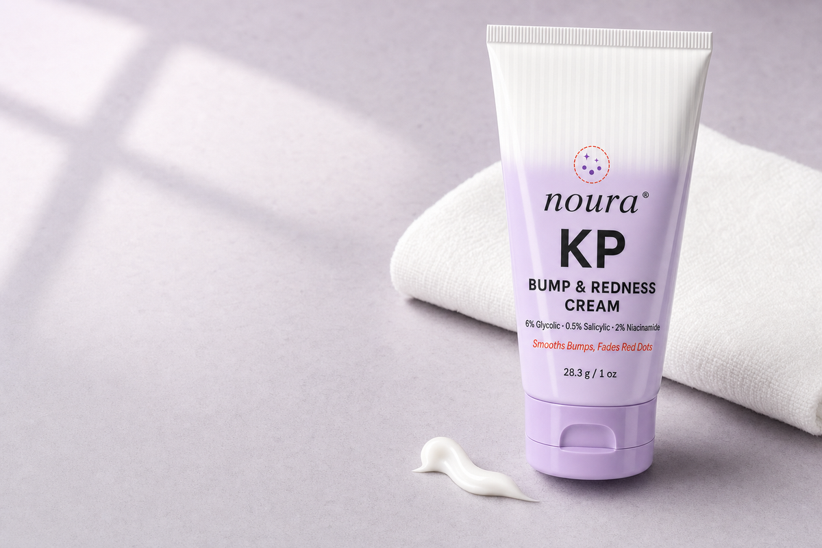 A tube of Noura KP Bump & Redness Cream beside a folded white towel, with a swirl of cream on the counter